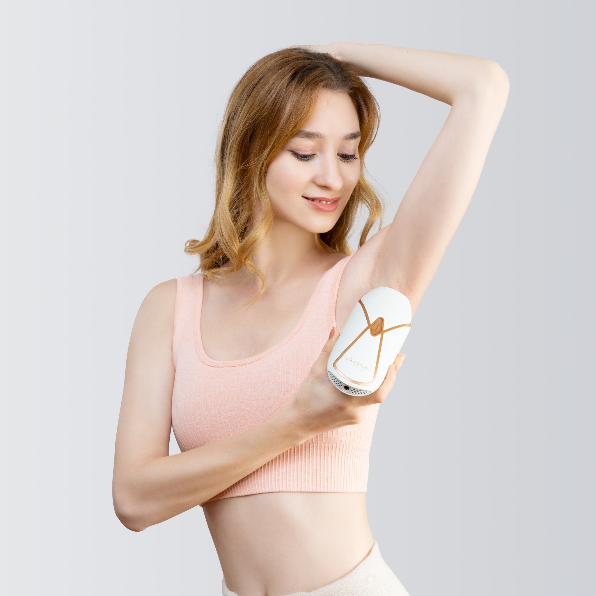 Product image of a beauty model wearing a pink crop top while using the Elegtime Sapphire IPL Hair Removal Handset - Troidini Edition on the underarm area.
